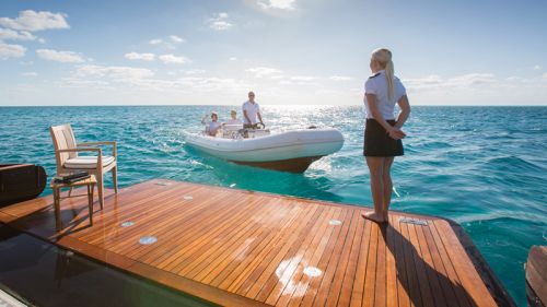 A stewardess standing on the swim platform of a yacht welcomes charter guests arriving by tender boat