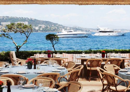 Tables set up for lunch on the terrace of La Gurite in Cannes with charter yachts at anchor