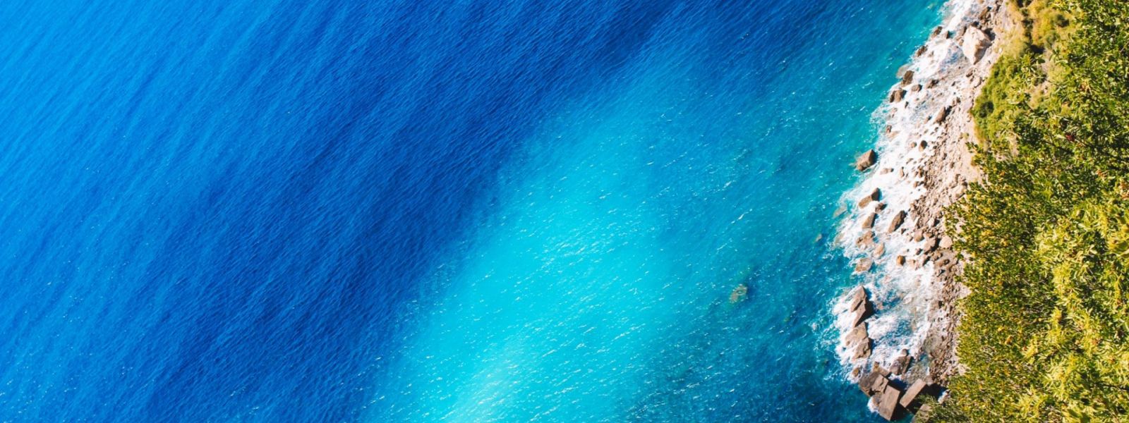 Aerial sea view with turquoise waters, pebbles beach and green vegetation