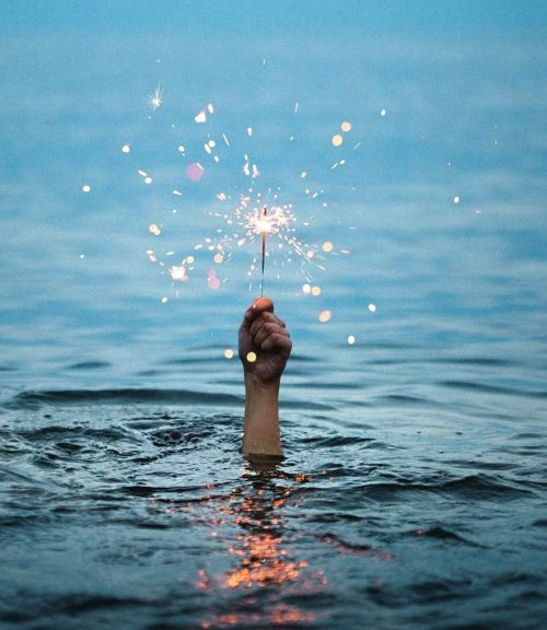 A hand holding sparklers in the sea 