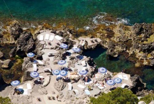 The beach restaurant La Fontelina in Capri with blue and white umbrellas, turquoise waters and people swimming