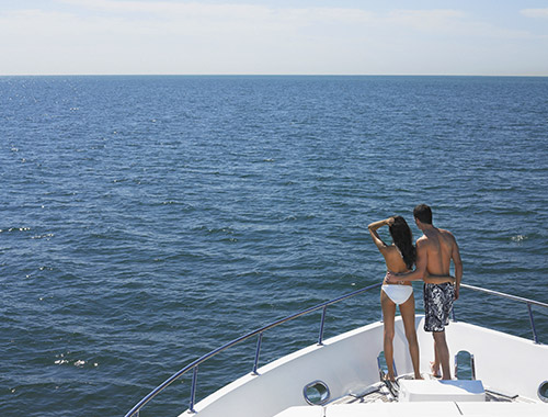 A couple in bathing suits standing at the bow of a charter yacht during their summer yachting holidays in the Mediterranean