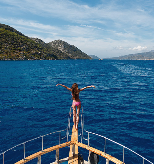 A woman in a bathing suit standing at the bow of a charter yacht in the Mediterranean