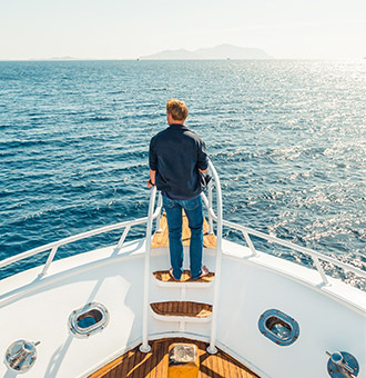 A yacht owner at the bow of his yacht gazing at the horizon